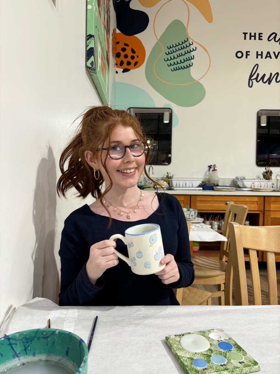 Keira Howell smiling and holding a mug, seated at a table