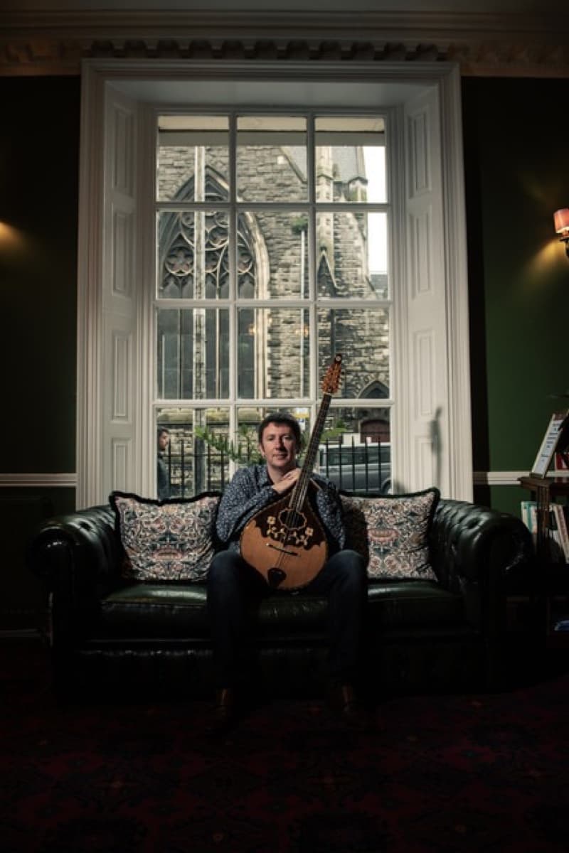 Irish folk singer Daoirí Farrell seated on a leather sofa holding a bouzouki