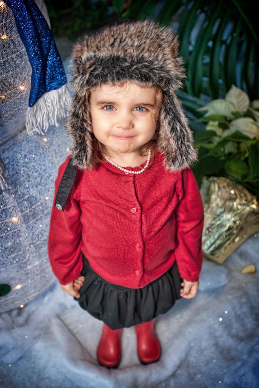 Lexi Townsin as a toddler in a fur hat and red cardigan, smiling in a snowy holiday scene
